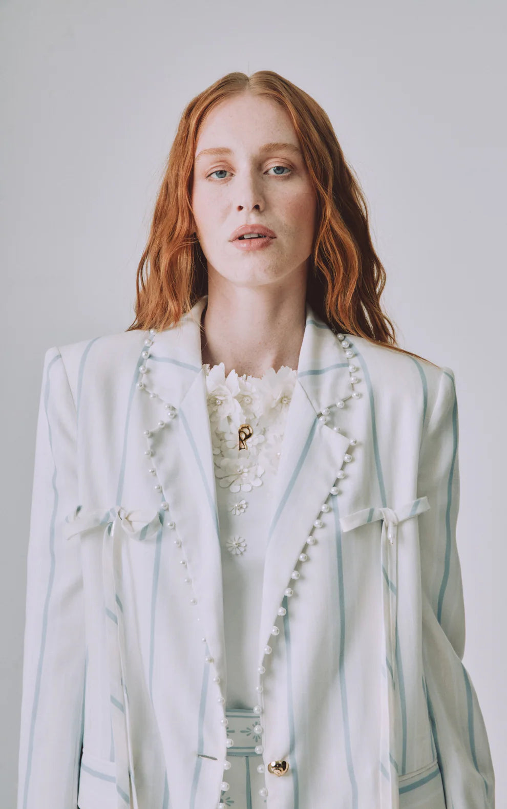 Woman wearing a light-colored blazer with floral details on a plain background