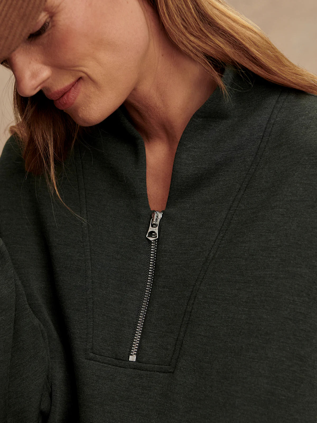 Close-up of a person wearing a dark gray zip-up sweatshirt with a beige background