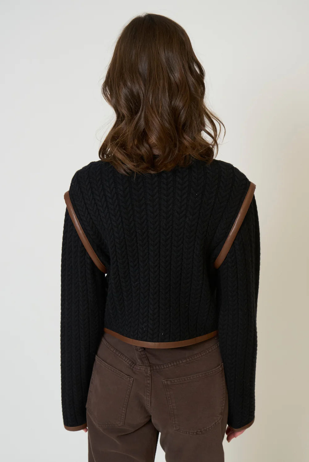 Person wearing a black sweater with brown accents on a plain background